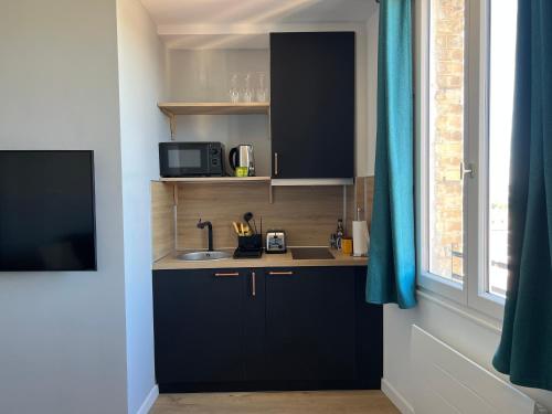 d'une cuisine avec des placards noirs, un évier et une fenêtre. dans l'établissement La vertindus - Centre ville, à Honfleur