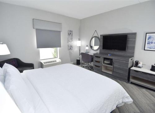 a hotel room with a white bed and a flat screen tv at Hampton Inn Auburn in Auburn