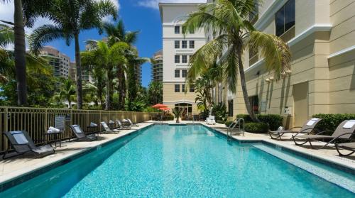 basen z krzesłami i palmami oraz budynek w obiekcie Hilton Garden Inn Palm Beach Gardens w mieście Palm Beach Gardens