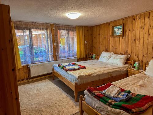 a bedroom with two beds and wooden walls and windows at Златкова къща in Koprivshtitsa