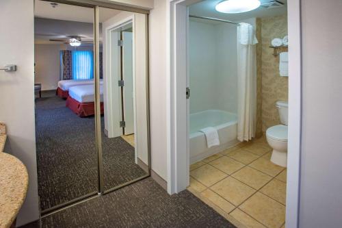 a bathroom with a toilet and a tub and a bedroom at Homewood Suites by Hilton Pensacola Airport-Cordova Mall Area in Pensacola