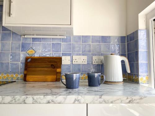 a kitchen counter with blue tiles and mugs on it at Swallows Drift in Newquay