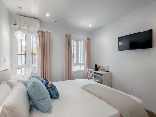 a white bedroom with a bed with a television on the wall at Hostal Perla Blanca Altea in Altea