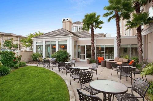 a patio with tables and chairs and palm trees at Hilton Garden Inn San Francisco Airport North in South San Francisco