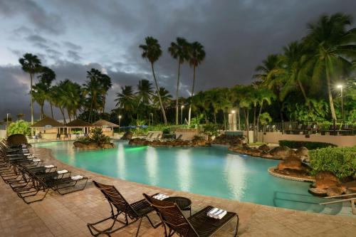 einen Pool in einem Resort mit Stühlen und Palmen in der Unterkunft Embassy Suites by Hilton San Juan - Hotel & Casino in San Juan