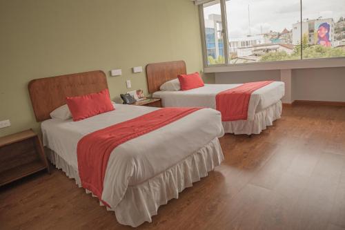 Habitación con 2 camas y sábanas rojas y blancas. en Hotel Ambato, en Ambato