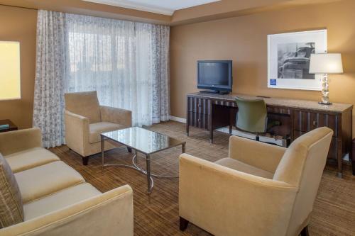 a living room with a television and chairs and a desk at Hilton St. Louis Airport in Woodson Terrace