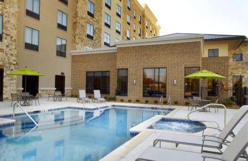 a pool with chairs and umbrellas next to a building at Hilton Garden Inn Texarkana in Texarkana - Texas