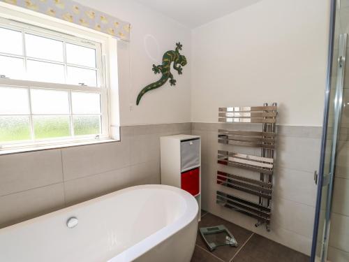 a bathroom with a tub and a window and a lizard on the wall at Larch House in Penrith