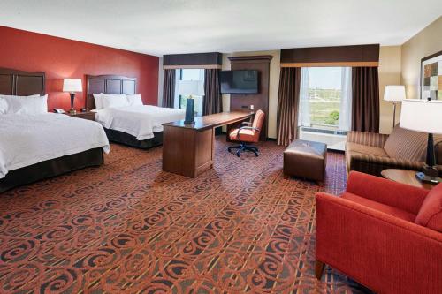 FranklinにあるHampton Inn & Suites Milwaukee/Franklinのベッド2台、デスク、ソファが備わるホテルルームです。