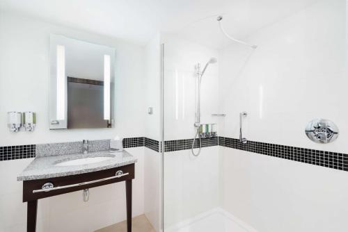 a white bathroom with a sink and a shower at Hampton by Hilton Krakow in Kraków