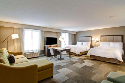 a hotel room with two beds and a couch at Hampton Inn & Suites by Hilton Saskatoon Airport in Saskatoon
