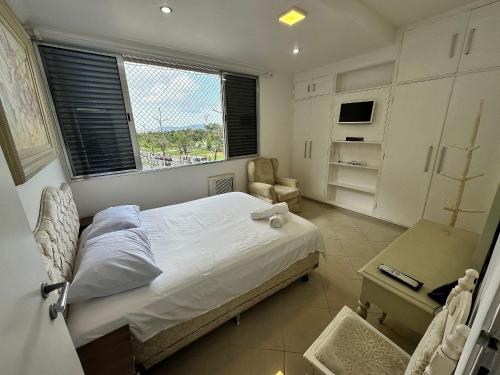a bedroom with a bed and a chair and a window at Frente Mar! 3 quartos e 2 vagas in Santos