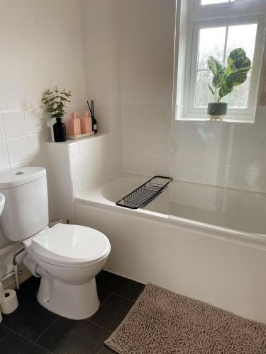 a white bathroom with a toilet and a bath tub at Cosy & stylish home from home in Peterborough