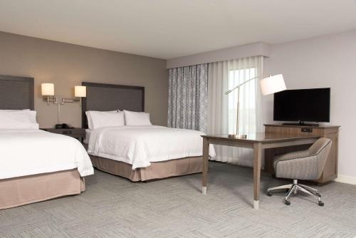 ein Hotelzimmer mit 2 Betten, einem Schreibtisch und einem TV in der Unterkunft Hampton Inn and Suites Michigan City in Michigan City