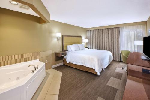 Hampton Inn Sault Ste Marie, MI في سولت سانت ماري: غرفة في الفندق مع سرير وحوض استحمام