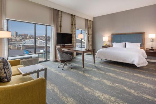 Habitación de hotel con cama y escritorio con TV. en Hampton Inn & Suites Newport/Cincinnati, KY en Newport
