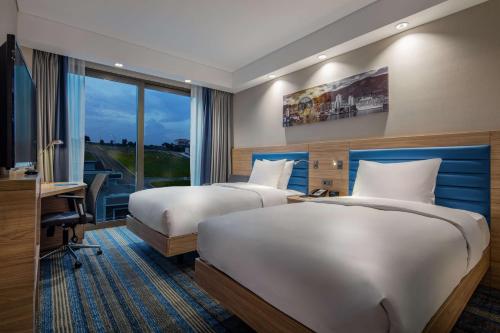 a hotel room with two beds and a desk and a window at Hampton By Hilton Izmir Aliaga in Aliağa