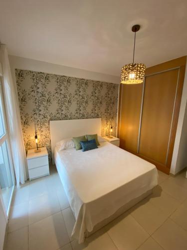 ein Schlafzimmer mit einem großen weißen Bett und einem Kronleuchter in der Unterkunft Lagunas Home, bajo con terraza al lado de la playa in Vera