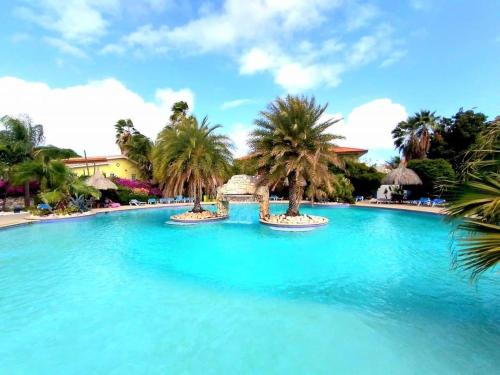 een zwembad met blauw water en palmbomen bij Kas di BaMi A-186 op Seru Coral Resort - Ruim appartement met groot zwembad en tropische tuin in Willemstad