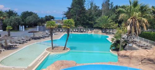 uma piscina num resort com palmeiras e cadeiras em Évasion océanique : Mobil-home dans un camping 4* à 50m de l'océan em La Bétaudière