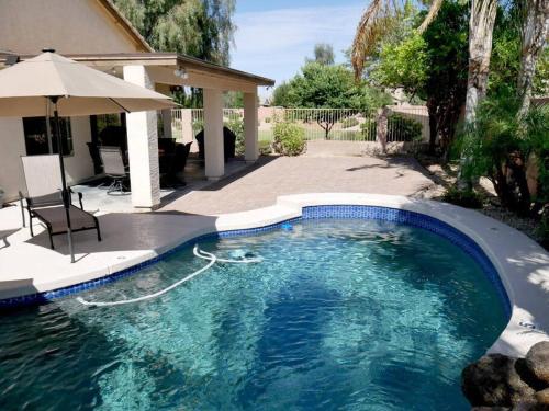 a swimming pool with an umbrella next to a house at Everything New! Ball Park Oasis With Heated Pool in Goodyear
