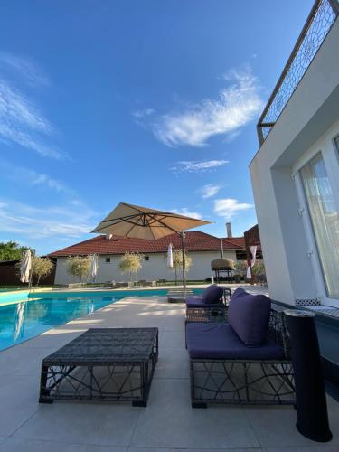 a patio with two couches and an umbrella next to a pool at CasaBlanca vendégház in Abádszalók