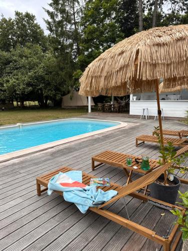 a deck with two chairs and a umbrella and a pool at Romantique petite chaumière près de Guérande in Saint-Lyphard