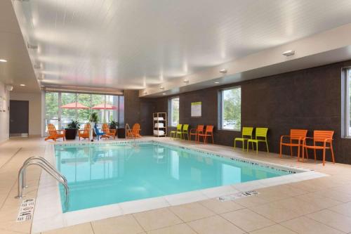 a pool in a hotel room with chairs and tables at Home2 Suites by Hilton Albany Airport/Wolf Rd in Albany