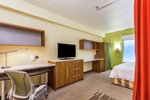 a hotel room with a bed and a desk with a television at Home2 Suites by Hilton Albany Airport/Wolf Rd in Albany