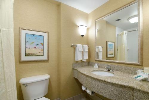 a bathroom with a toilet and a sink and a mirror at Hilton Garden Inn Outer Banks/Kitty Hawk in Kitty Hawk