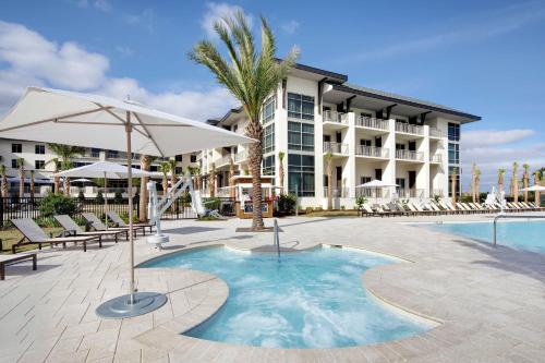 a pool with chairs and an umbrella and a hotel at Embassy Suites St Augustine Beach Oceanfront Resort in Saint Augustine Beach