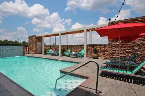 a swimming pool with chairs and an umbrella at Home2 Suites by Hilton Mobile I-65 Government Boulevard in Mobile