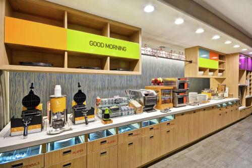 a restaurant with a counter with food items on it at Home2 Suites Plano Legacy West in Plano