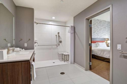 a bathroom with a sink and a shower and a bed at Home2 Suites By Hilton Bedford Dfw West in Bedford