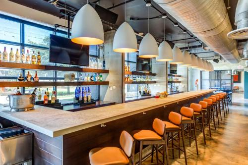 a bar with orange stools in a room with windows at NYLO Las Colinas Hotel, Tapestry Collection by Hilton in Irving