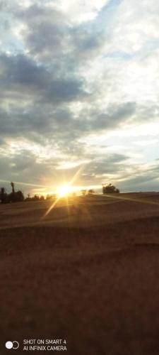 a sunset in the middle of a field with the sun setting at Sahara Camp Light in Mhamid