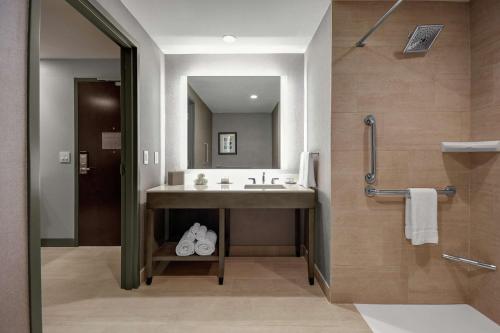 a bathroom with a sink and a mirror and a shower at Embassy Suites Jonesboro - Arkansas State in Jonesboro