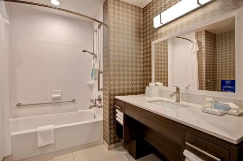 a bathroom with a tub and a sink and a mirror at Home2 Suites By Hilton Loves Park Rockford in Loves Park