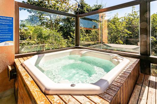 a jacuzzi tub on a wooden deck with windows at Resort pé na areia - Studios direto com proprietário JBVJR in Florianópolis