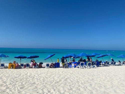 a group of people sitting on a beach with blue umbrellas at شالية استوديو 52 متر in Marsa Matruh