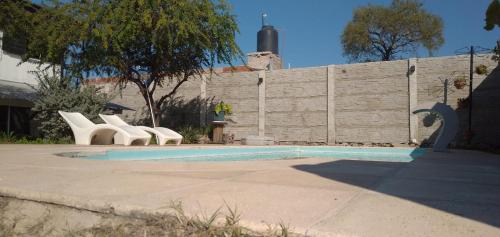 - une piscine avec des chaises blanches et un mur dans l'établissement Cabaña Raices, à Unquillo