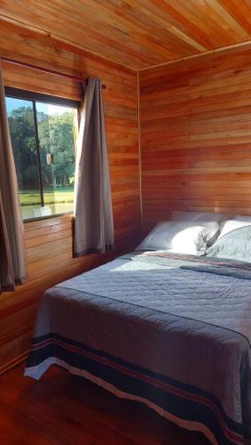 a bed in a wooden room with a window at Cabana Entre Lagos in São Joaquim