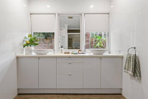 a white bathroom with two sinks and two windows at The Pod in Peregian Beach