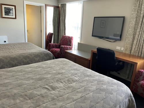 a hotel room with two beds and a desk and a television at Discovery Settlers Hotel in Whangarei