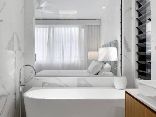 a white bathroom with a tub and a mirror at Luxury with lake and hinterland views in Noosa Heads