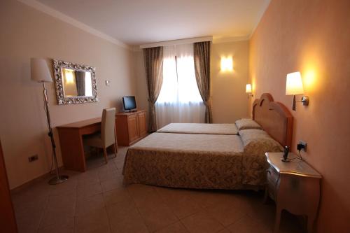 una camera con letto, scrivania e specchio di Hotel La Perla a Àrbatax