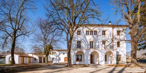una gran casa blanca con árboles delante de ella en Can Passarells, en San Vicente de Torelló