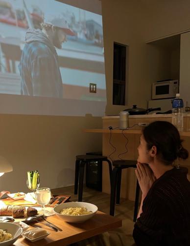 a woman sitting at a table watching a movie at HOLLY CAMP CASA in Akagina