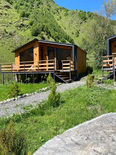 a wooden cabin in a field with a mountain at Little Wood House Gergeti in Stepantsminda
